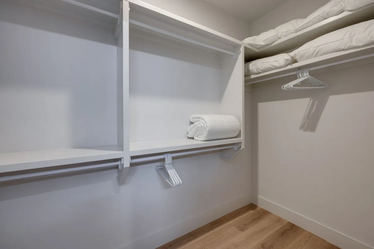 An organized and calming closet space with shelves, rolled towels, and pillows, evoking a sense of order and comfort. The soft, neutral tones suggest a restful retreat.