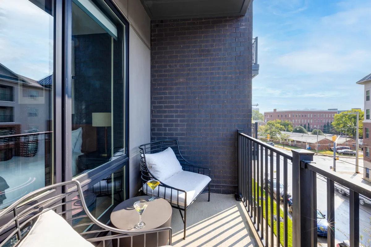 A private balcony setup with comfortable seating and a table, overlooking the vibrant city below. The scene evokes relaxation, with a drink set on the table and the energy of the city visible from above.
