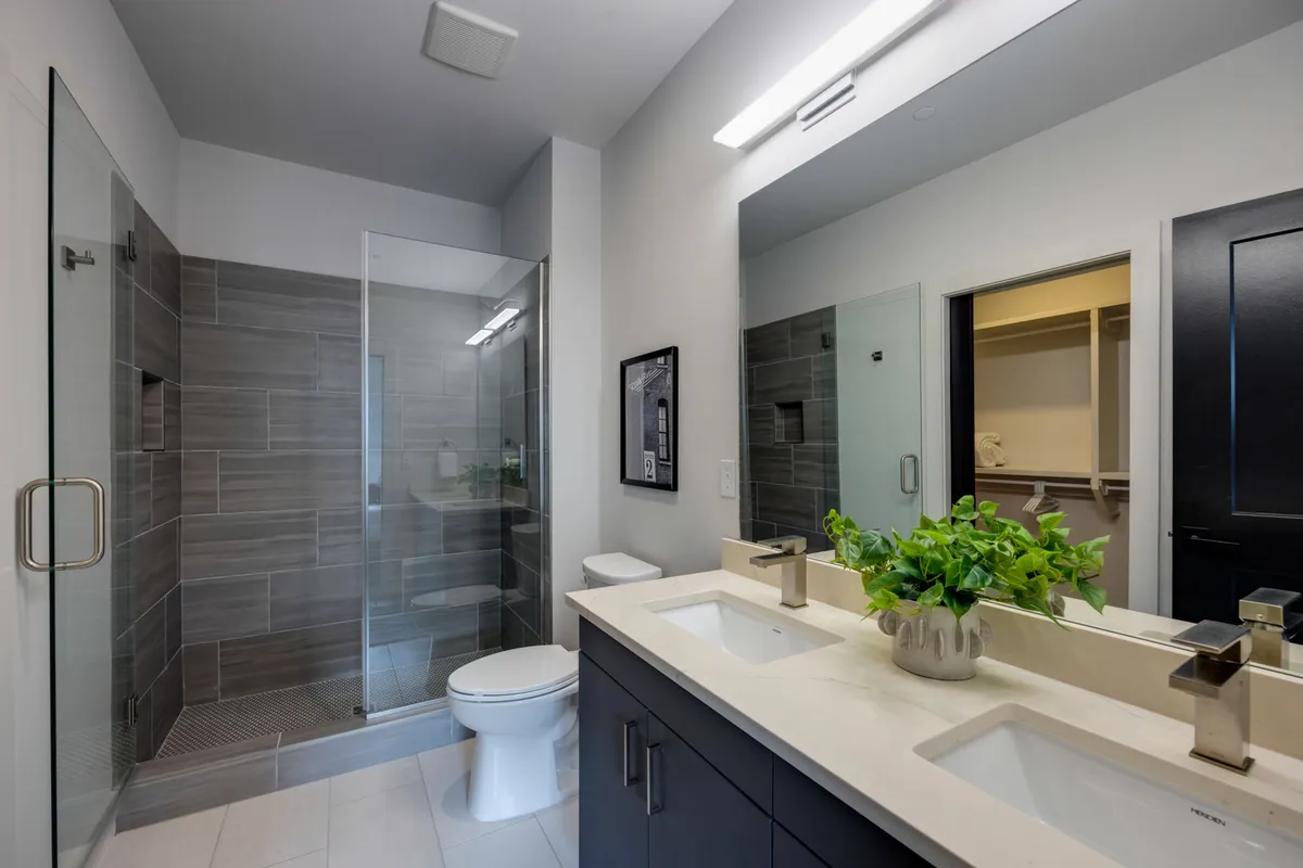 A luxurious bathroom scene with a double sink vanity, glass-enclosed shower, modern fixtures, and plant decor. The overall style is fresh and tranquil, perfect for spa-inspired relaxation.