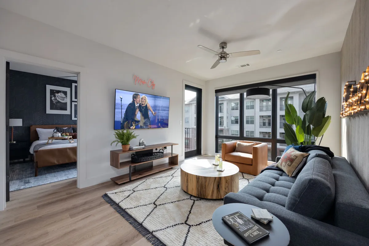 The image showcases a stylish, modern living area with a plush sofa, contemporary coffee table, a large TV for entertainment, and a touch of greenery from a well-placed plant. The space exudes comfort, inviting guests to relax, watch movies, or enjoy intimate conversations.